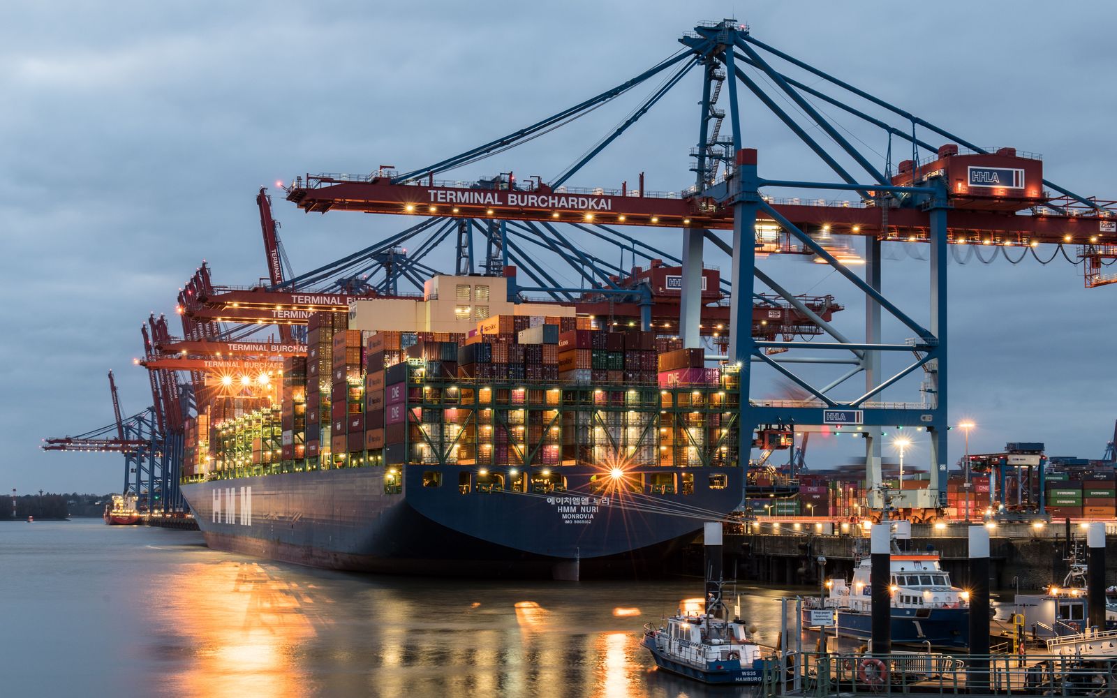 Container ship loaded with cargo containers under port cranes at dusk