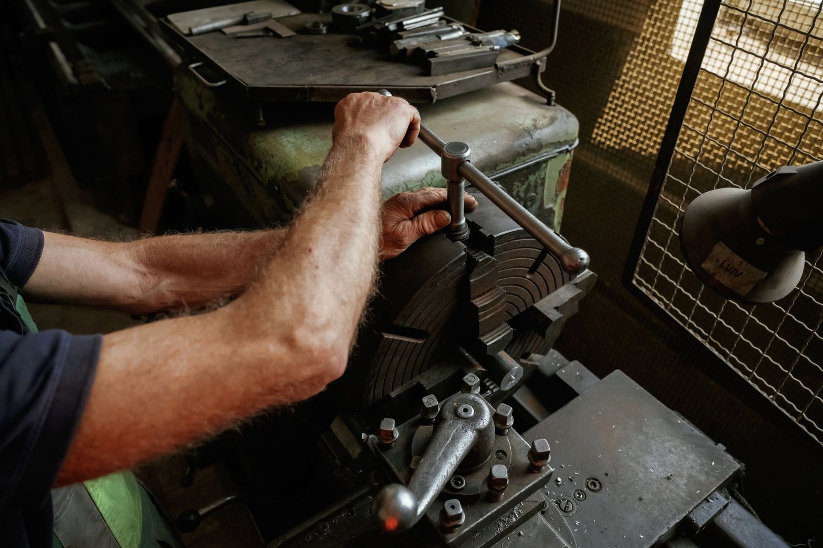A worker's hands turning the handle of an old metal machine on a factory floor