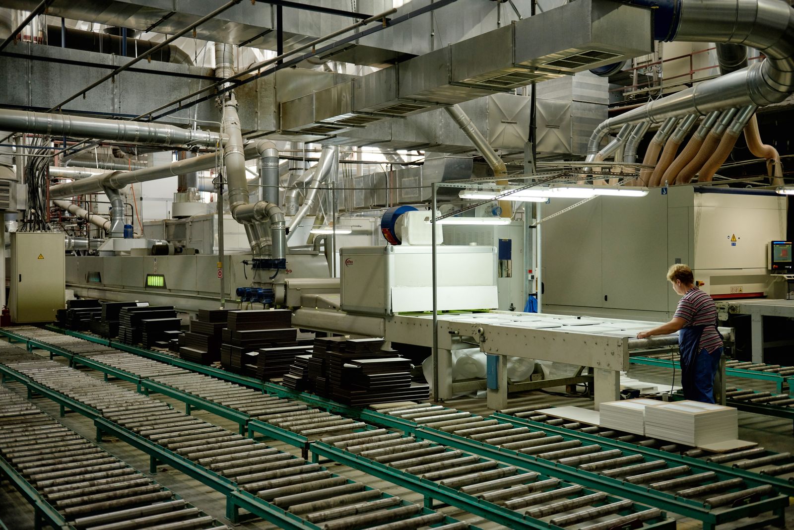 Factory production line with roller conveyors, machines and overhead ducts, one worker at a station