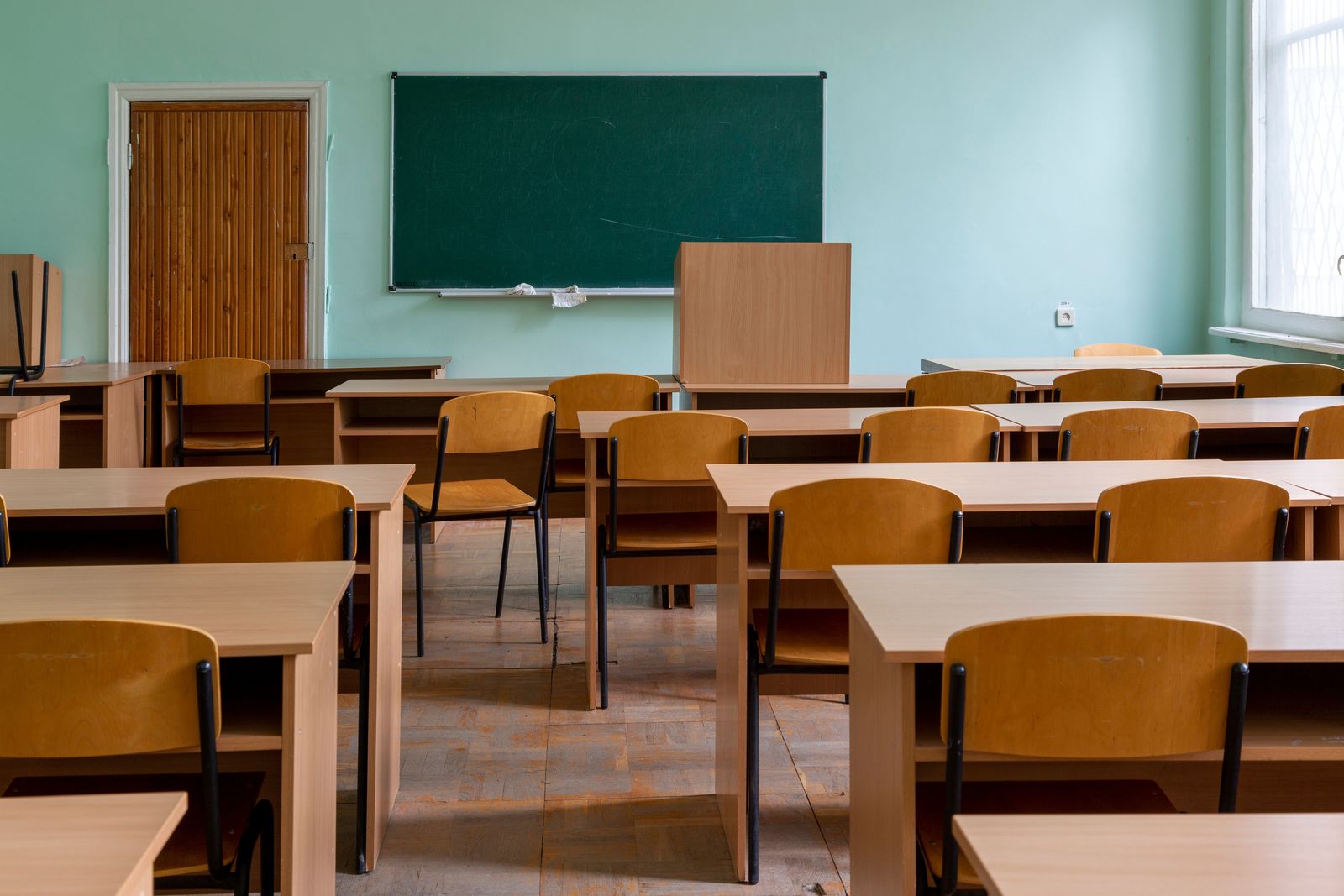 Empty school classroom with rows of wooden desks and chairs facing a green chalkboard